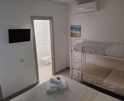 A cozy hostel room with bunk beds, neatly folded towels on a bed, a mounted TV, and an en-suite bathroom visible through an open door, ideal for budget travelers seeking comfort and convenience.