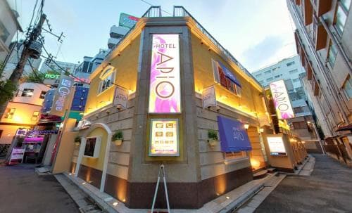 A warmly lit hotel corner in an urban alleyway exudes a cozy, inviting atmosphere with its vibrant signage and potted plants, perfect for travelers seeking a charming accommodation spot in a bustling city.