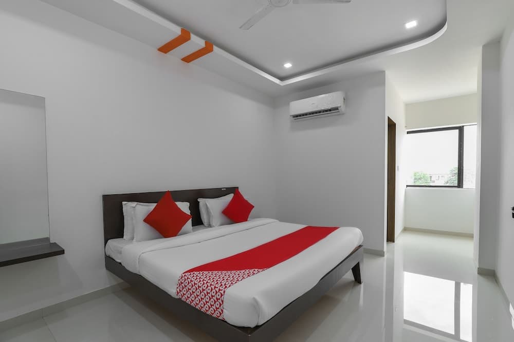 A modern hotel room features a neatly made bed with red accents, sleek white decor, and a balcony view, ideal for travelers seeking comfort and style.