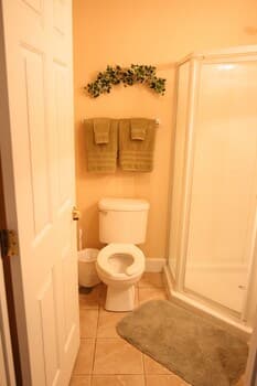 A cozy bathroom with tiled floors, a toilet adorned with green towels, a glass-enclosed shower, and a festive wreath above, ideal for travelers seeking comfort and cleanliness in their accommodations.
