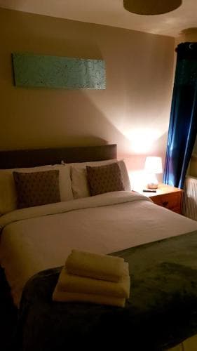 A cozy hotel room features a neatly made bed with soft lighting, a folded towel on a chair, and a modern bedside lamp, ideal for travelers seeking comfort and relaxation.