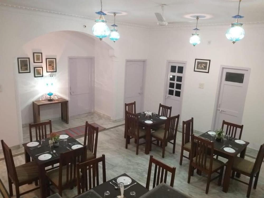 A cozy indoor dining area with marble floors, wooden tables set for meals, blue glass pendant lights, and framed artwork creates an inviting atmosphere ideal for travelers seeking a comfortable and intimate restaurant experience.
