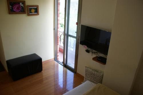 A cozy apartment interior features a wooden floor, a flat-screen TV, and a glass door leading to a balcony, ideal for travelers seeking a comfortable urban retreat.