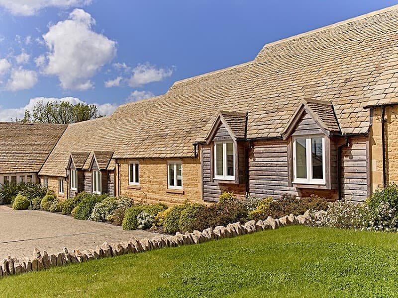 A serene countryside retreat featuring charming timber-framed cottages under a clear blue sky, ideal for travelers seeking a peaceful rural escape in the Cotswolds.