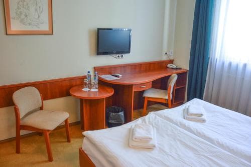A cozy hotel room features a neatly made bed, wooden furniture, and a mounted TV, creating a welcoming atmosphere ideal for travelers seeking comfort and convenience.