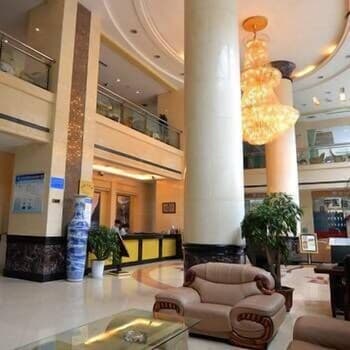 A luxurious hotel lobby features elegant seating, marble columns, and a glowing chandelier, creating a welcoming atmosphere ideal for travelers seeking comfort and sophistication.