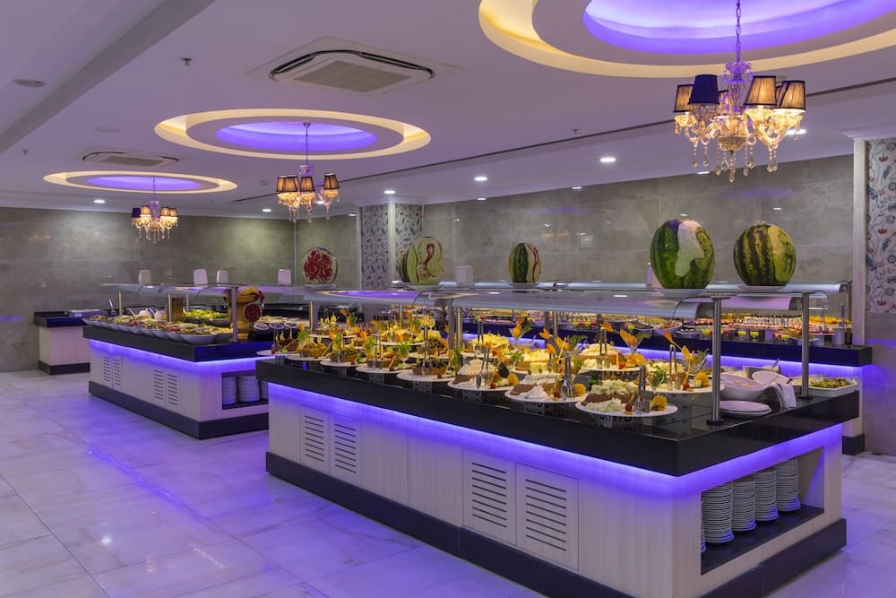 A vibrant buffet restaurant with purple-lit counters, chandeliers, and decorative watermelons creates an inviting atmosphere ideal for travelers seeking a luxurious dining experience.