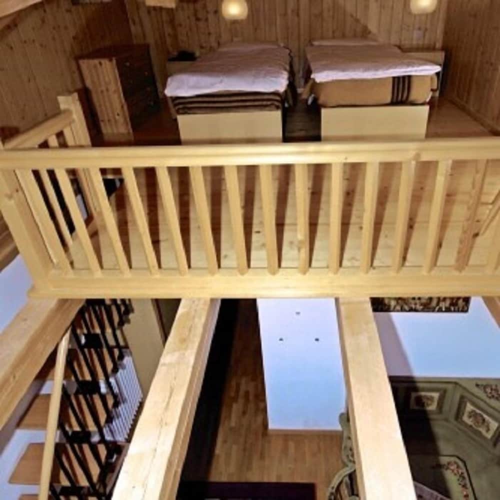 A cozy loft bedroom with wooden railings overlooks a warmly lit living space below, ideal for travelers seeking a rustic and intimate accommodation experience.
