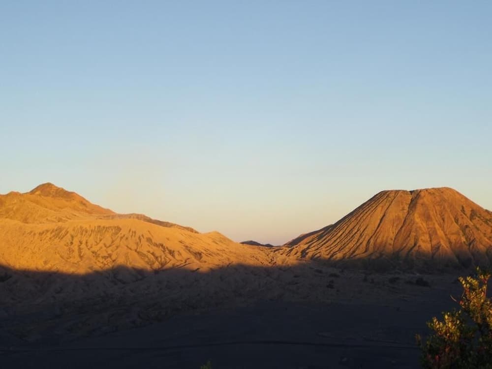 A serene volcanic landscape bathed in golden sunset light, featuring rugged mountains and a dark sandy foreground, ideal for adventure seekers exploring natural wonders.