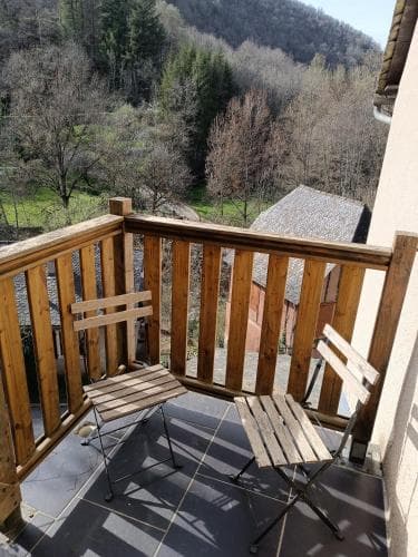 A cozy balcony with wooden railings and chairs overlooks a serene forested valley, ideal for travelers seeking a peaceful retreat in nature.