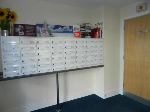 A cozy office corner features organized white mailboxes on a shelf adorned with books and vibrant sunflowers, creating a welcoming atmosphere ideal for business travelers seeking efficient communication solutions.