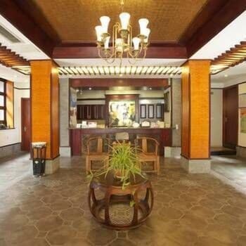 A warmly lit traditional lobby with wooden pillars, a central plant table, and elegant chandeliers creates an inviting atmosphere ideal for travelers seeking cultural immersion in a heritage hotel setting.