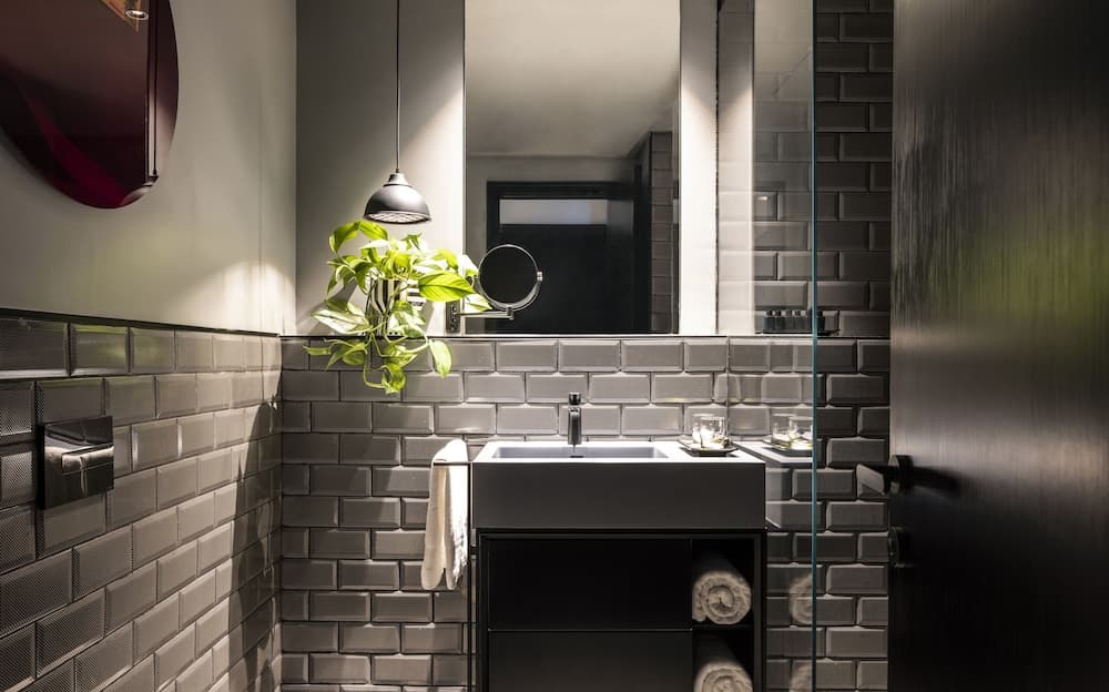 A modern bathroom with sleek gray brick tiles, a minimalist sink setup, and a hanging plant creates a serene and stylish atmosphere, ideal for travelers seeking upscale accommodations.