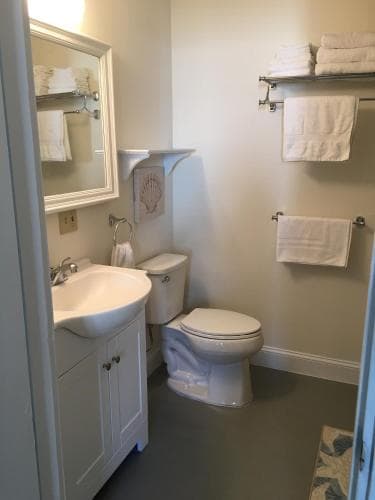 A cozy, well-organized bathroom features a white vanity, toilet, and neatly folded towels on shelves, creating a clean and inviting atmosphere ideal for travelers seeking comfort in accommodations.