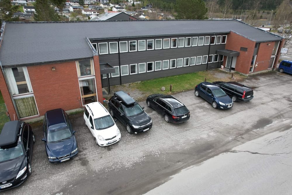 A serene suburban office building with parked cars in front, surrounded by greenery and residential houses, ideal for business travelers seeking a quiet work environment.