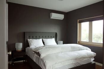 A cozy bedroom with dark walls, a neatly made bed, and natural light streaming through a window, ideal for travelers seeking a serene and comfortable stay.