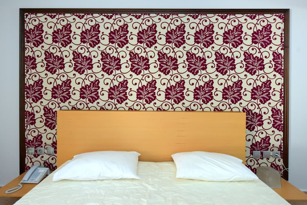 A cozy hotel room features a neatly made bed with white linens against a decorative floral-patterned headboard, ideal for travelers seeking comfort and style.