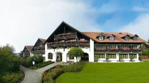 A charming alpine lodge with flower-adorned balconies stands amidst lush greenery under a serene sky, ideal for travelers seeking a cozy retreat in a picturesque mountain setting.