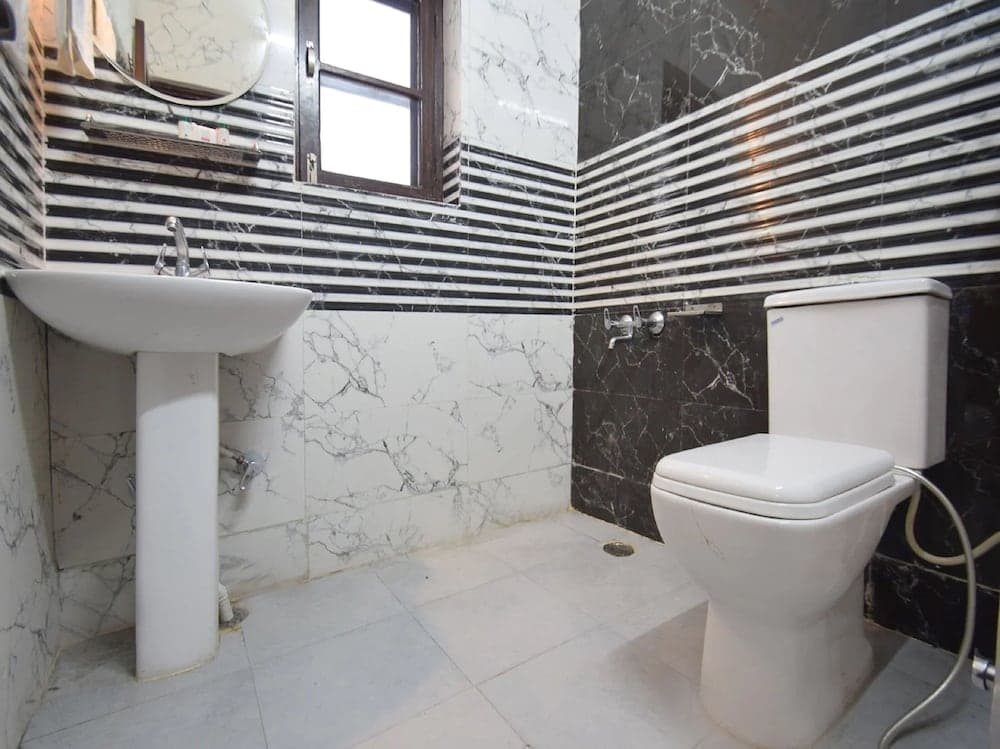A modern bathroom with black and white marble tiles, featuring a pedestal sink, toilet, and window, exudes a clean and stylish ambiance ideal for travelers seeking comfort in accommodations.
