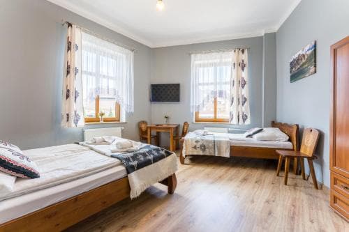 A cozy, well-lit guesthouse room with wooden beds, patterned textiles, and large windows offers a serene retreat for travelers seeking comfort and simplicity.