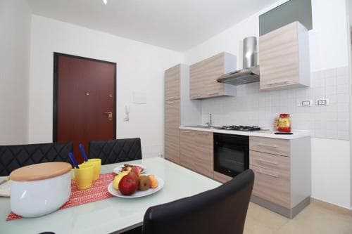 A cozy apartment kitchen with modern wooden cabinets, a dining table set with fresh fruit, and a warm ambiance ideal for travelers seeking a comfortable self-catering stay.