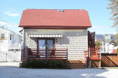 A charming beachside cottage with a red roof and wooden deck invites travelers seeking a cozy seaside retreat, perfect for family vacations or weekend getaways.