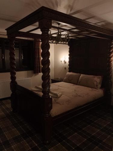 A cozy hotel room features an ornate four-poster bed with intricate woodwork, set against warm-toned walls adorned with a chandelier and wall sconces, ideal for travelers seeking a charming and intimate stay.