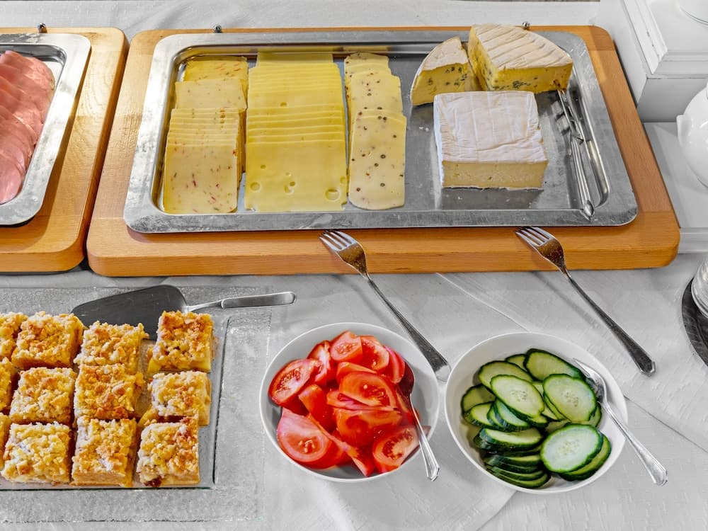 A vibrant breakfast buffet scene featuring an assortment of cheeses, fresh vegetables, pastries, and meats on a neatly arranged table, ideal for travelers seeking a hearty morning meal in a cozy dining setting.