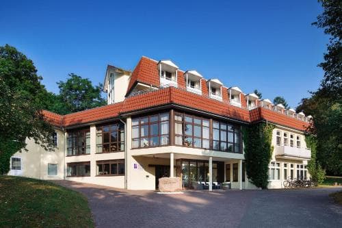 A serene countryside hotel with a red-tiled roof and glass facade stands amidst lush greenery, offering travelers a tranquil retreat with scenic views and outdoor amenities like bicycles for exploration.