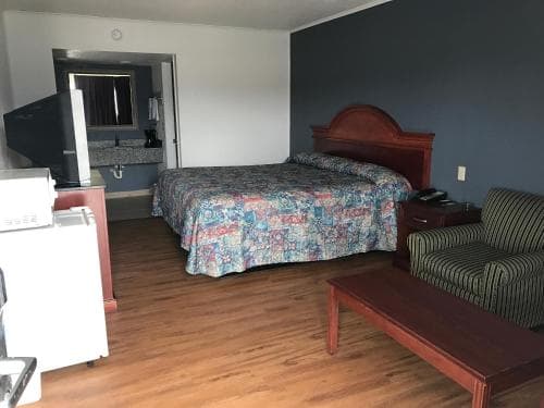 A cozy motel room features a neatly made bed with a floral comforter, wooden furniture, and a small seating area, ideal for travelers seeking a comfortable and budget-friendly stay.
