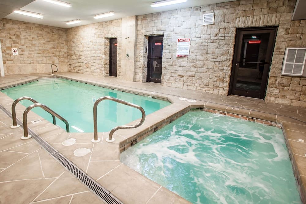 A serene indoor pool area features a tranquil swimming pool adjacent to a bubbling hot tub, surrounded by stone walls and equipped with metal railings, ideal for relaxation and leisure in a resort or hotel setting.