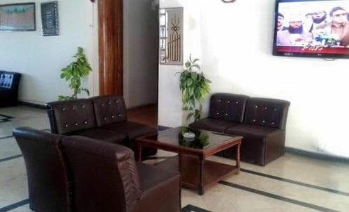 A cozy hotel lobby features brown leather sofas arranged around a wooden coffee table, complemented by potted plants and a wall-mounted TV, creating a welcoming atmosphere ideal for travelers seeking relaxation.