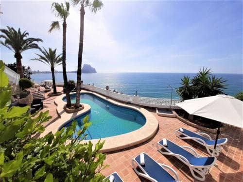 A serene coastal resort features a kidney-shaped pool surrounded by lounge chairs, palm trees, and a breathtaking ocean view, ideal for relaxing beachside vacations.