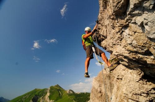 A climber ascends a rugged cliff face under a clear blue sky, showcasing an adventurous outdoor activity ideal for thrill-seekers exploring mountainous regions.