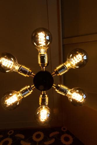 A warmly lit indoor space features an artistic chandelier with multiple glowing bulbs, creating a cozy ambiance ideal for boutique hotels or design-focused travel experiences.