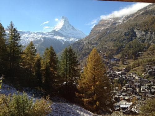 A picturesque alpine village nestled among golden autumn trees and towering snow-capped mountains offers a serene retreat for hikers and nature enthusiasts.