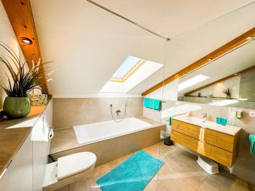 A cozy attic bathroom with a skylight, wooden accents, and modern fixtures offers a serene retreat, ideal for travelers seeking relaxation in a unique space.