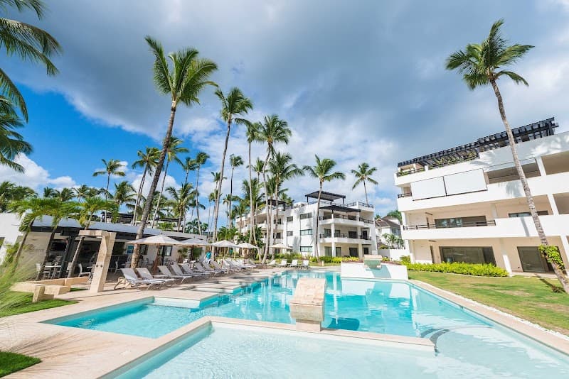 A serene tropical resort scene featuring a sparkling pool surrounded by lounge chairs and palm trees under a partly cloudy sky, ideal for a relaxing vacation getaway in Las Terrenas, Dominican Republic.