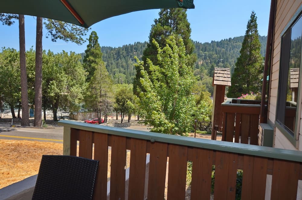 A serene balcony view offers a cozy retreat with wooden railings, lush greenery, and distant hills, ideal for travelers seeking relaxation in a forested mountain getaway.