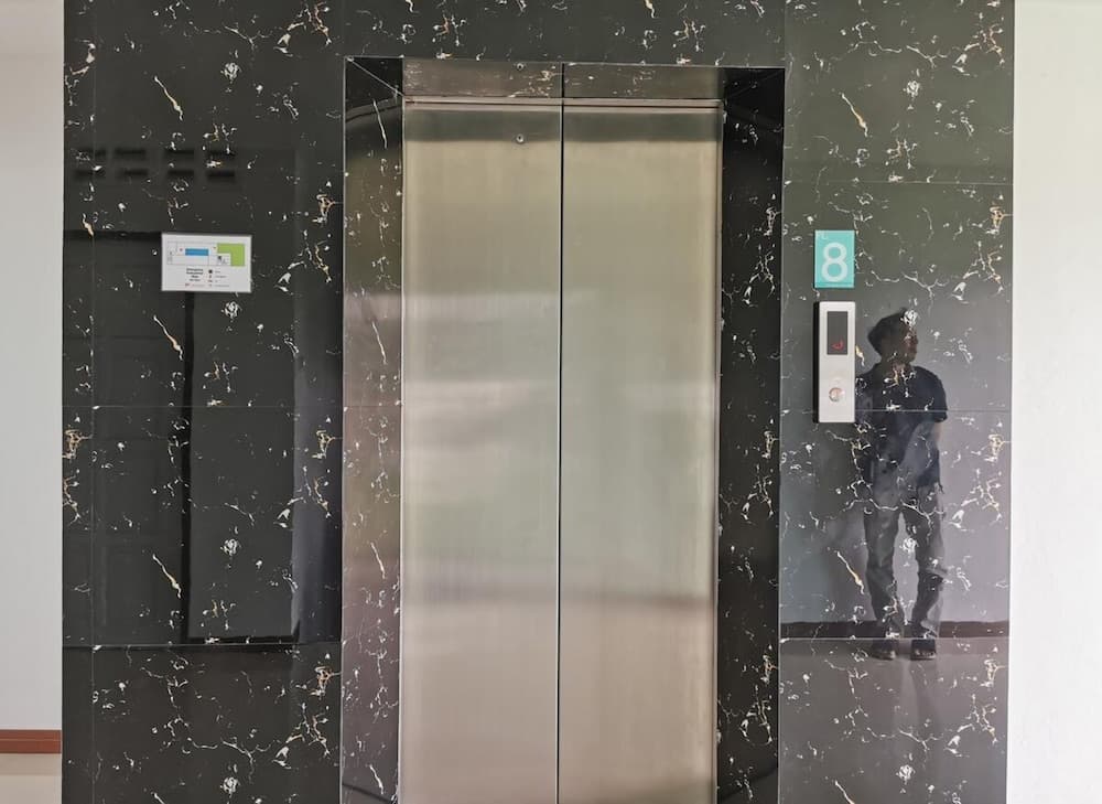 A sleek elevator with stainless steel doors framed by black marble walls reflects a person's silhouette, creating a modern and sophisticated atmosphere ideal for business travelers seeking upscale accommodations.