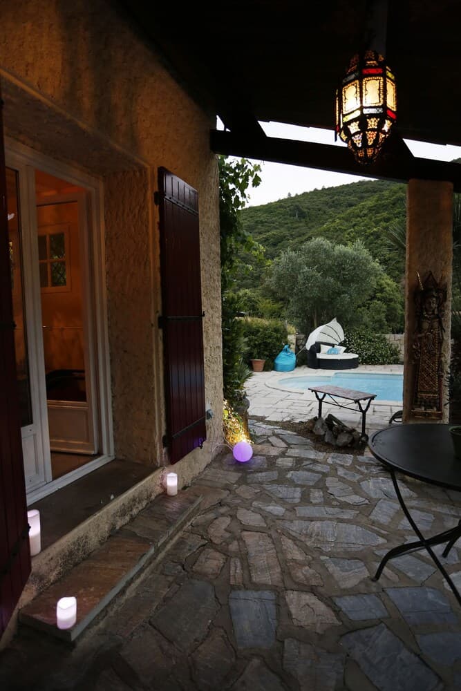 A cozy stone patio adorned with candles and a lantern overlooks a serene pool surrounded by lush greenery, ideal for a tranquil retreat or romantic getaway.