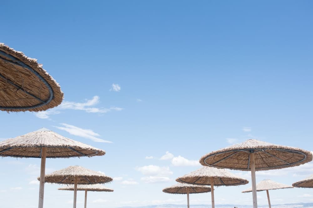 A serene beach scene features straw umbrellas under a clear blue sky, ideal for travelers seeking relaxation and sunbathing spots.