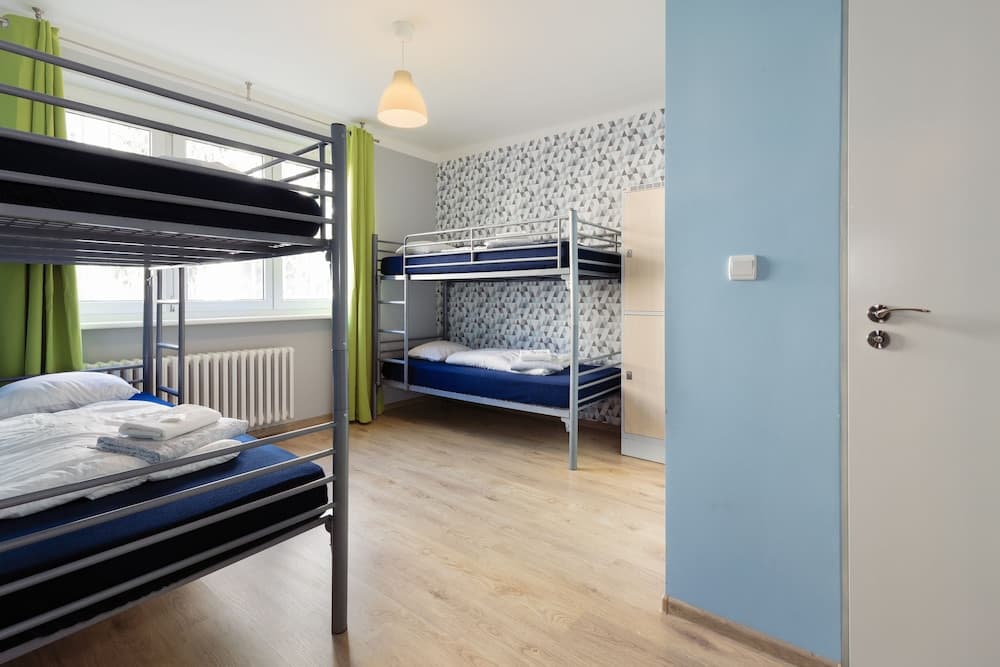 A cozy hostel room with bunk beds, green curtains, and patterned wallpaper offers a welcoming atmosphere for budget travelers seeking comfortable accommodations.
