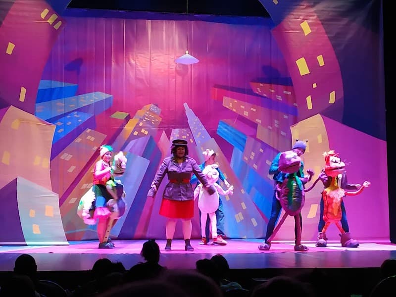 A vibrant theatrical performance unfolds on the stage of Teatro Apolo in Miranda de Ebro, Spain, featuring colorful costumes and playful characters against a whimsical cityscape backdrop, ideal for family entertainment and cultural exploration.