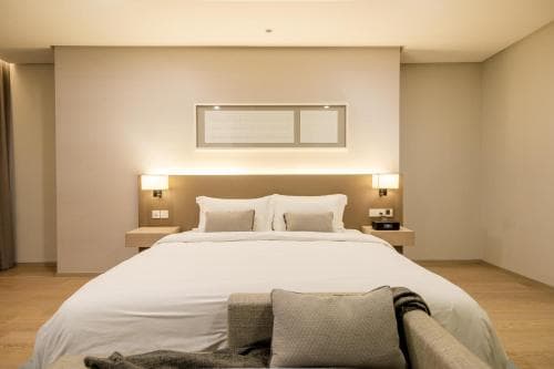A serene hotel room features a cozy bed with white linens, modern bedside lamps, and a minimalist design, ideal for travelers seeking relaxation and comfort.