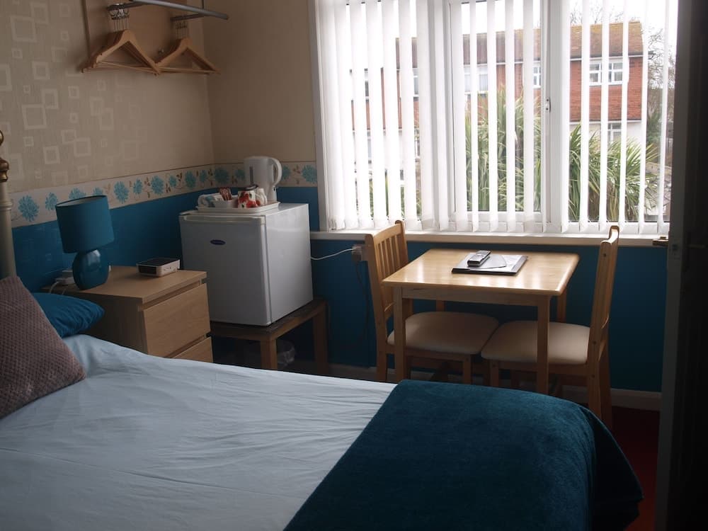 A cozy hotel room with a neatly made bed, wooden furniture, a mini-fridge, and a bright window view of greenery, ideal for travelers seeking comfort and convenience.
