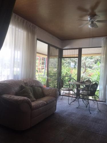 A cozy sunroom with a plush sofa, glass doors leading to lush greenery, and a metal table set for relaxation, ideal for travelers seeking a tranquil retreat in a vacation rental.