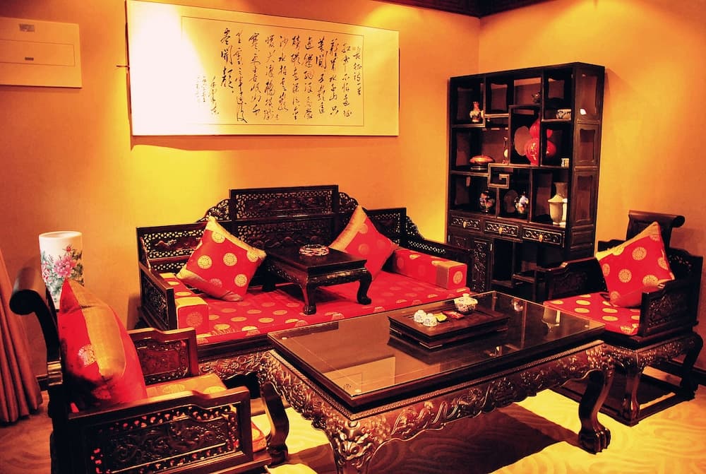 A warmly lit traditional Chinese living room features intricate wooden furniture, red patterned cushions, a glass-topped table, and decorative shelves, creating an inviting atmosphere ideal for cultural exploration and interior design inspiration.