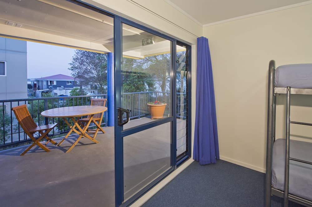 A cozy apartment balcony with wooden furniture and a potted plant offers a serene view of residential rooftops, ideal for travelers seeking a peaceful retreat.