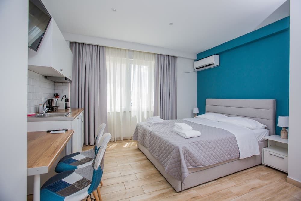A cozy hotel room with a neatly made bed, blue accent wall, modern kitchenette, and soft lighting creates a welcoming atmosphere ideal for travelers seeking comfort and convenience.